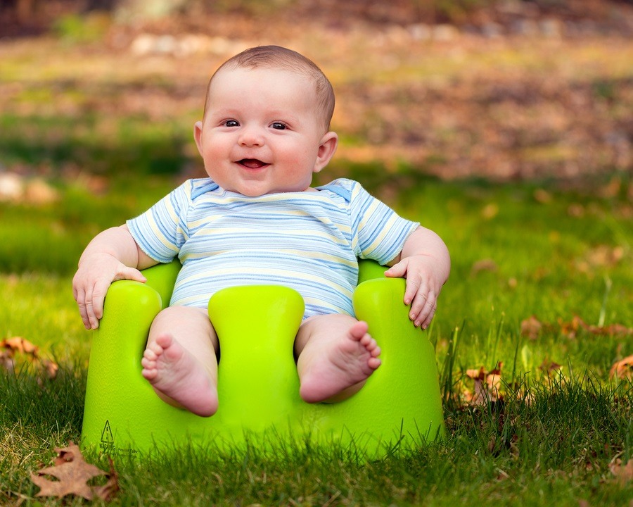 Happy infant baby boy using training Bumbo seat to sit up